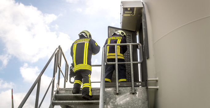 Auf diesem Bild sieht man wie die Feuerwehr eine Windkraftanlage betritt.