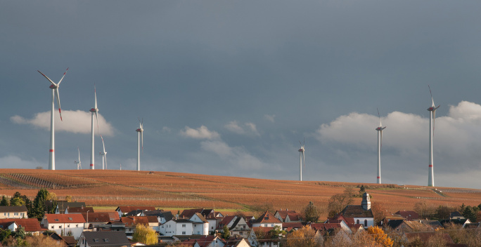 ein kleinse Dorf ist zu sehen, im Hintergrund sieht man auf einem Feld Windräder stehen